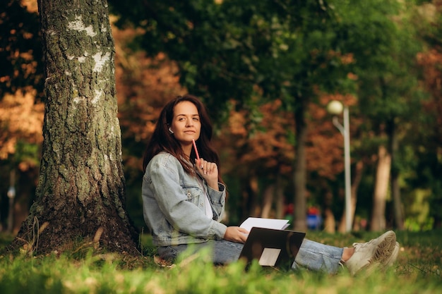 Frau studiert und macht Notizen, während sie mit einem Laptop im Park sitzt