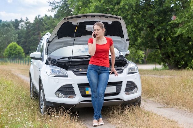 Frau stützte sich auf kaputtes auto im feld und ruft auf dem handy um hilfe