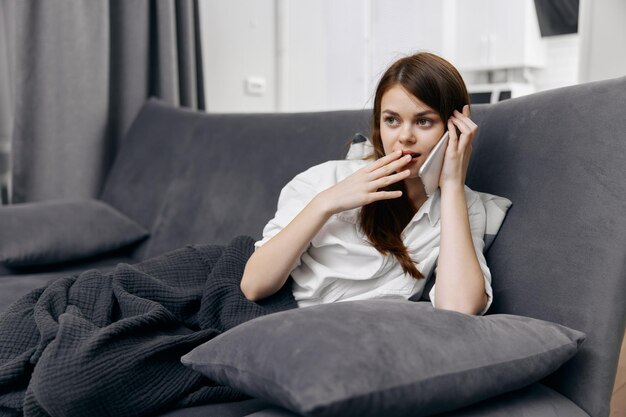 Frau telefoniert und sitzt mit einer Decke auf dem Schoß auf der Couch