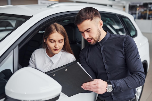 Frau testet Auto mit Hilfe eines männlichen Assistenten, der Domente drinnen im Salon zeigt.