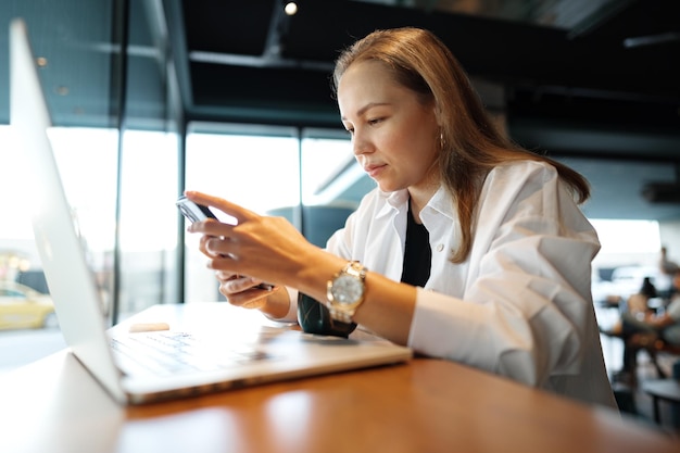 Frau tippt Textnachricht auf Smartphone, während sie in einem Café sitzt