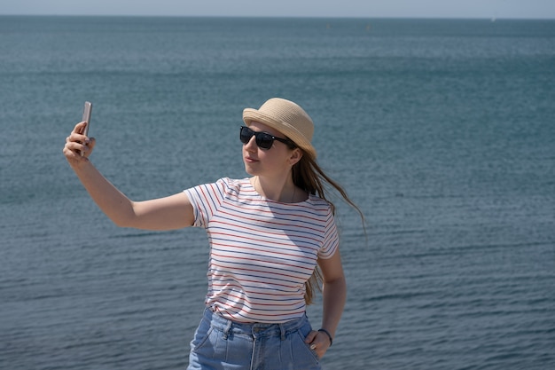 Frau Tourist in Freizeitkleidung macht Selfie mit dem Telefon am Meer. Ruhe im Ausland, Seeluft. Nahansicht.