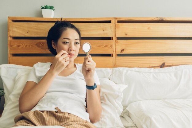 Frau trägt Make-up auf ihrem Bett im Schlafzimmer.