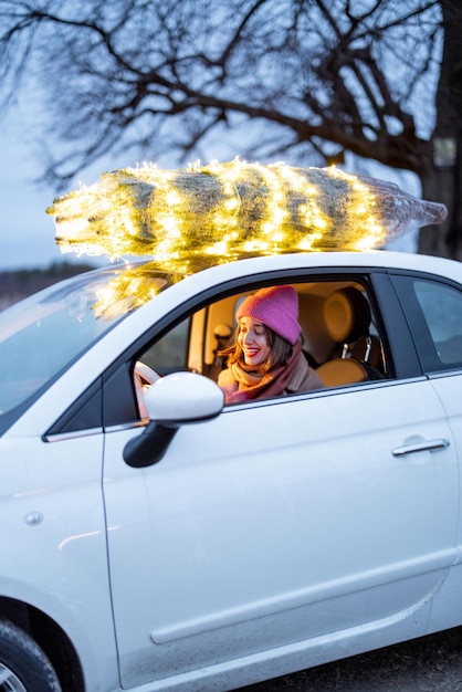 Frau trägt Weihnachtsbaum im Auto