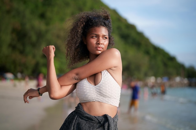 Frau trainiert und dehnt Muskeln vor dem Training im Freien Portrait sexy asiatische afrikanische Dame bereitet sich auf Fitness am Strand vor