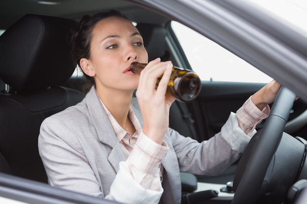 Frau trinkt Bier beim Autofahren