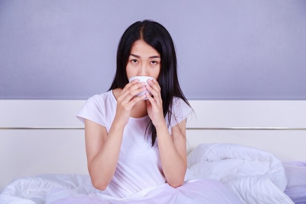 Frau trinkt eine Tasse Kaffee auf dem Bett im Schlafzimmer