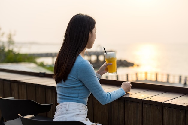 Frau trinkt eine Tasse saftiges Kaffee im Freien bei Sonnenuntergang