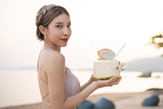 Frau trinkt frische Kokosnuss am Strand, romantischer Sonnenuntergangsmoment. Sommerurlaub.