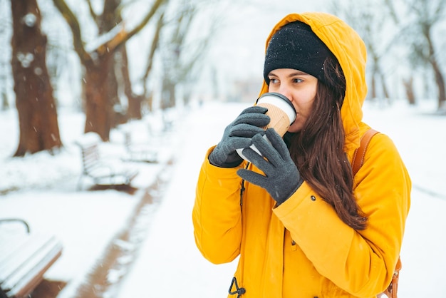Frau trinkt Kaffee draußen im Park Porträtgetränk zum Aufwärmen im Winter