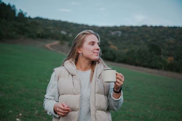 Frau trinkt Kaffee im Campingstuhl im Wald Wanderkonzept