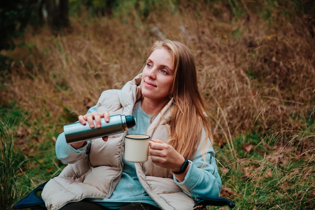 Frau trinkt Kaffee im Campingstuhl im Wald Wanderkonzept