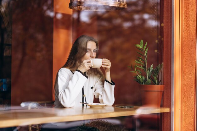 Foto frau trinkt kaffee in einem café und sitzt hinter dem glas