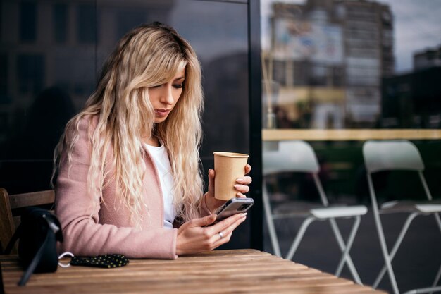 Frau trinkt Kaffee und hält Telefon draußen