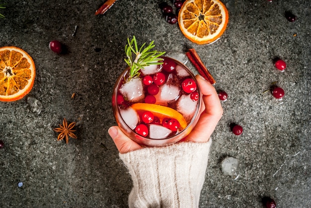 Frau trinkt kaltes Cocktail mit Moosbeeren, Orange, Rosmarin und Gewürzen