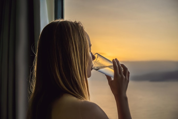 Frau trinkt morgens Wasser auf dem Hintergrund eines Fensters mit Meerblick