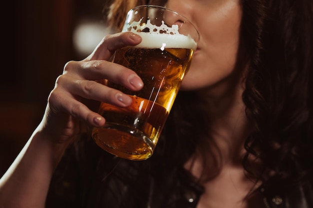 Frau trinkt sexuell aus einem Glas Bier mit Schaum