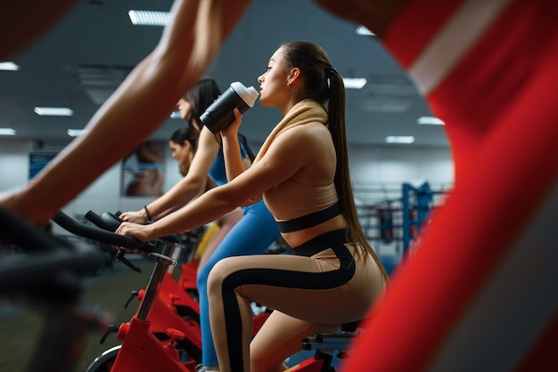 Frau trinkt Wasser auf einem stationären Fahrrad im Fitnessstudio. Leute beim Fitnesstraining im Sportclub
