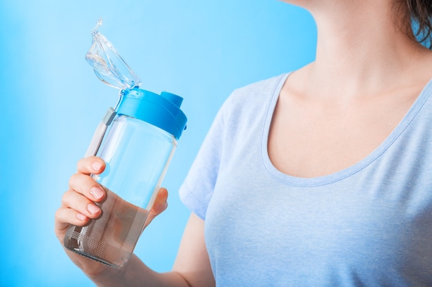Frau trinkt Wasser aus der Flasche für den Sport auf der wiederverwendbaren Flasche der blauen Wand gesunder Lebensstil und Fitnesskonzept