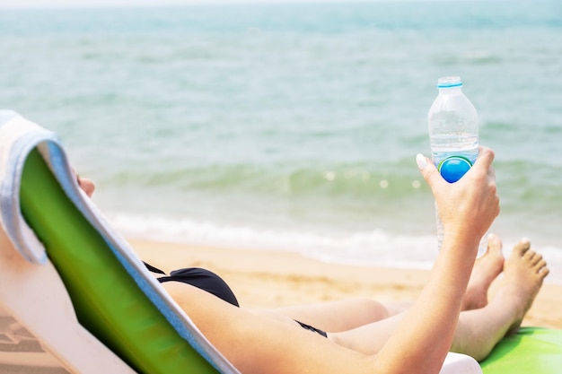 Frau trinkt Wasser und ruht auf einer Sonnenliege am Strand