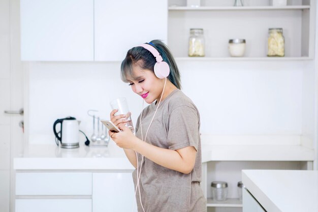 Frau trinkt Wasser, während sie Musik in der Küche genießt