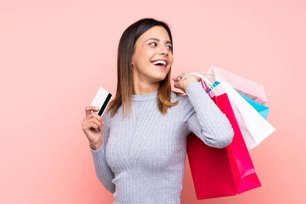 Frau über der rosa Wand, die Einkaufstaschen und eine Kreditkarte hält
