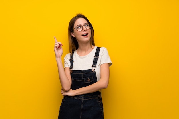 Frau über gelber Wand eine Idee denkend, die oben den Finger zeigt