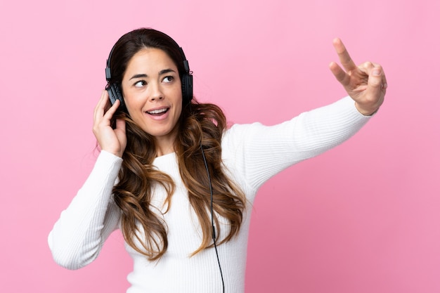 Frau über isolierte rosa Wand, die Musik hört und singt