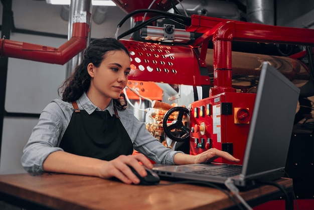 Frau überprüft seinen Laptop, während sie einen modernen Kaffeeröster bedient