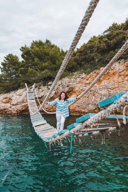 Frau überquert Hängebrücke Meer im Hintergrund Sommerzeit