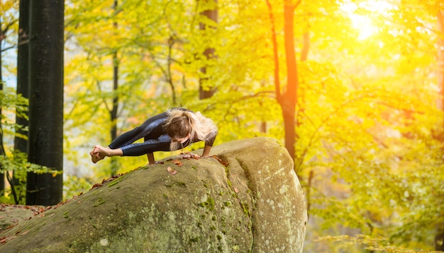 Frau übt Yoga im Herbstwald auf dem großen Stein