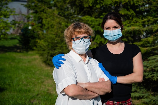 Frau umarmt eine ältere Mutter, die zum Schutz vor dem Virus medizinische Masken trägt. Eine Rentnerin und ihre erwachsene Tochter gehen während der Coronavirus-Epidemie im Park spazieren