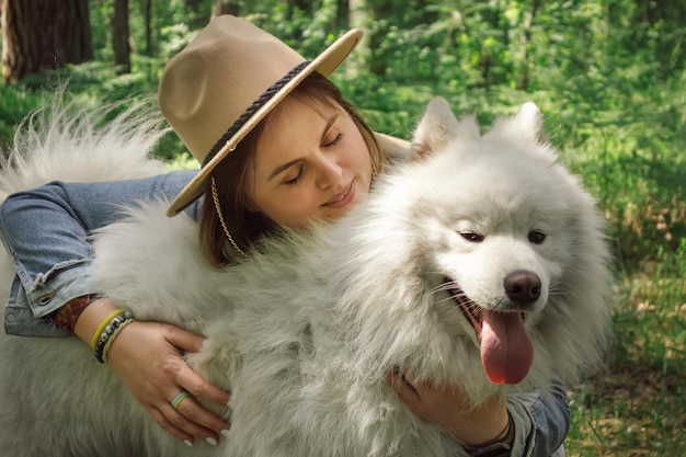 Frau umarmt ihren Hund Samoyed im Wald