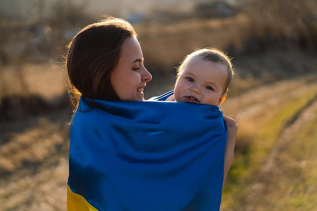 Frau umarmt ihren kleinen sohn, eingewickelt in die gelbe und blaue flagge der ukraine im freien