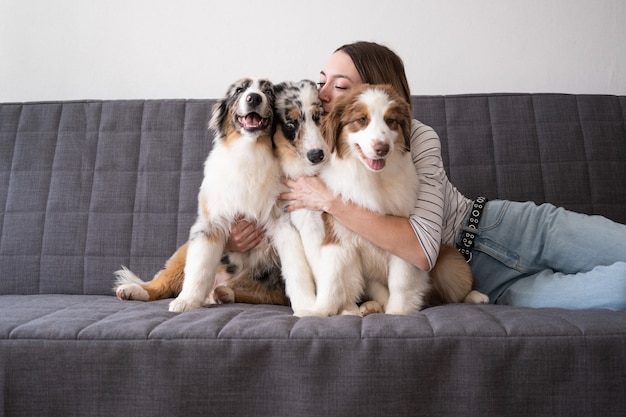 Frau umarmt mit drei Merle-Farben Australian Shepherd Welpe Hund auf der Couch