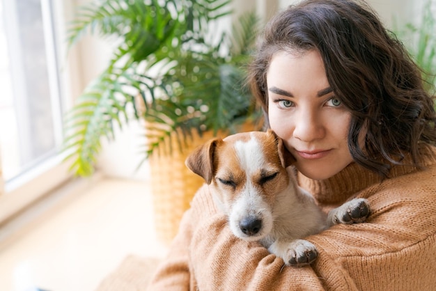 Frau umarmt süßen kleinen Hund, der zu Hause in ihren Armen liegt Closeup Trust