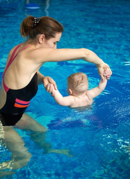 Frau und Baby, die Übungen machen, die in aufrechter Position in einem flachen Pool schwimmen Verhärtung und Krankheitsprävention Rückansicht