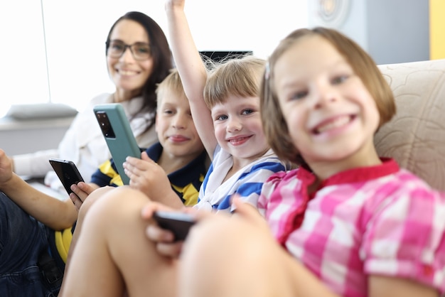Frau und drei Kinder sitzen auf der Couch, lächeln und halten Smartphones in ihren Händen.