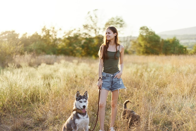 Frau und ihr Husky gehen glücklich im Gras auf dem Feld spazieren und rennen, lächeln mit Zähnen, Herbstsonnenuntergang, Spaziergang mit einem Haustier, das mit einem Freund reist, Hundeglück