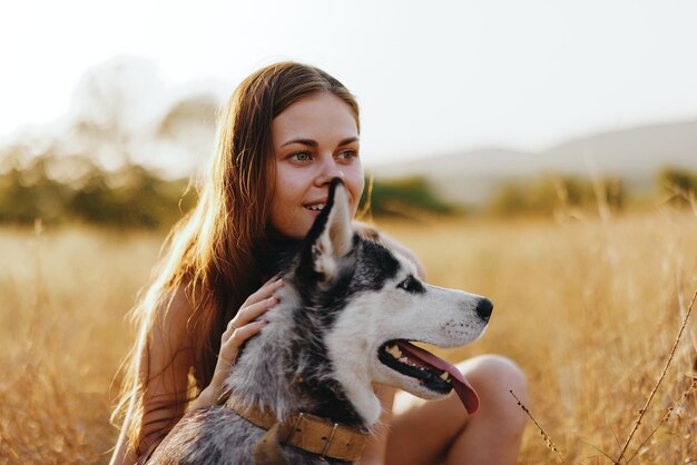 Frau und ihr Husky schlendern glücklich durch das Gras im Park, lächeln mit Zähnen, Herbstsonnenuntergangsspaziergang mit Haustier, reisen mit einem Hundefreund