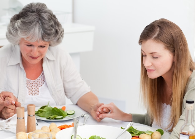 Frau und ihre Mutter, die am Tisch beten