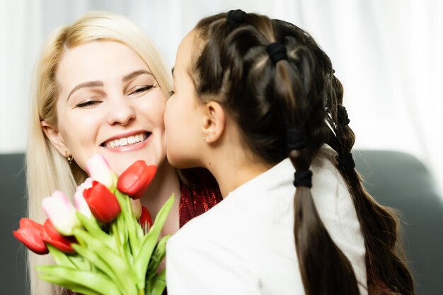 Frau und Kind mit Blumenstrauß vor häuslichem Hintergrund. Familienurlaubskonzept im Frühling. Frauentag.