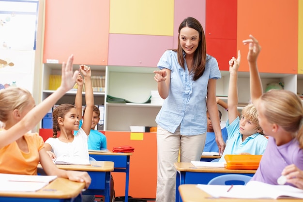 Frau und Kinder mit erhobenen Händen in der Klasse für Bildung Diskussion und Antwortwahl Glücklicher Lehrer und Schüler mit Geste in der Schule für Lernbeteiligung und Lösung