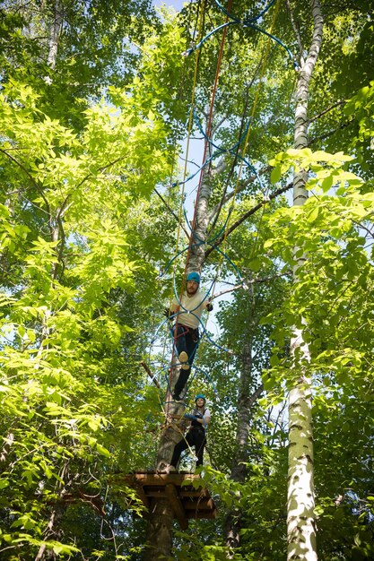 Frau und Mann haben eine Seilunterhaltung im grünen Wald, die hoch steht und auf der Seilbrücke geht