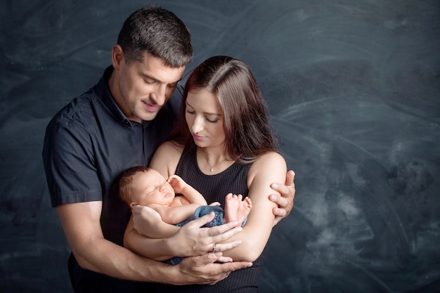 Frau und Mann halten ein Neugeborenes. Mama, Papa und Baby. Nahansicht. Porträt der lächelnden Familie mit Neugeborenem an den Händen.