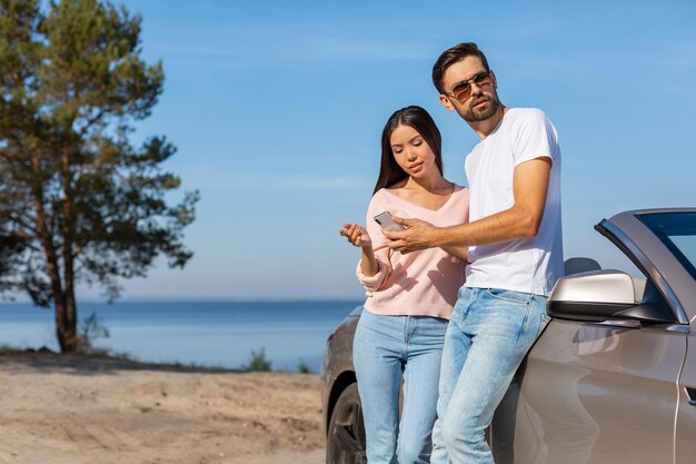 Frau und Mann stehen am Auto und benutzen Smartphone