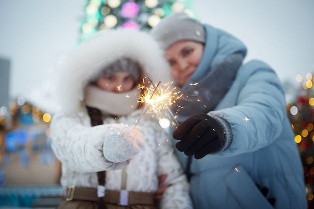 Frau und Teenager-Mädchen mit Weihnachtswunderkerzen in Winterkleidung auf der Straße.