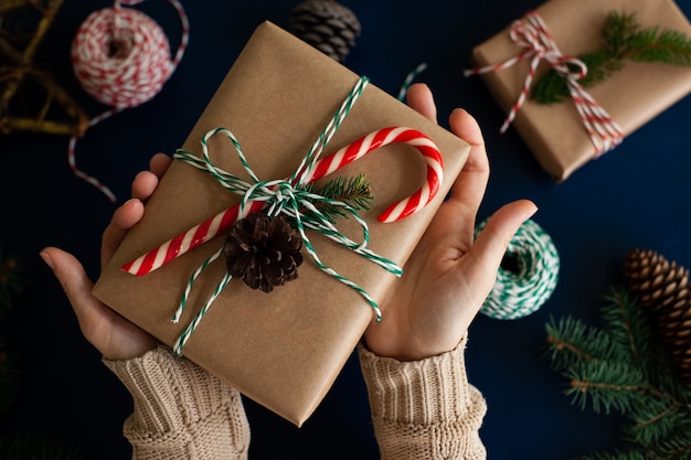 Foto frau verpackt ein handgemachtes weihnachtsgeschenk im öko-stil in kraftpapier und natürlichen fichtenzweigen auf blauem holzhintergrund.