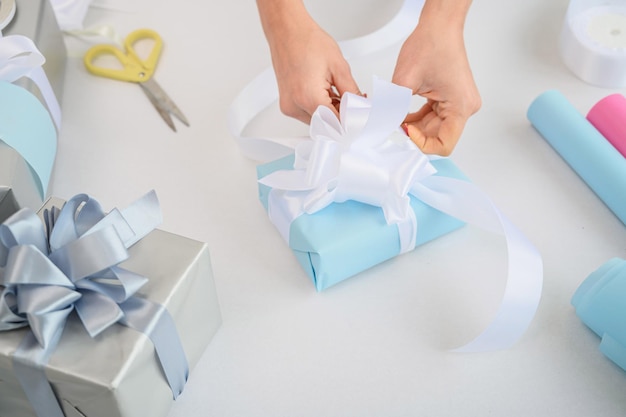 Frau verpackt Kisten mit Geschenken für das neue Jahr. Nahaufnahme weiblicher Hände bereitet eine Überraschung für Weihnachten vor. Geschenkpapier und Band