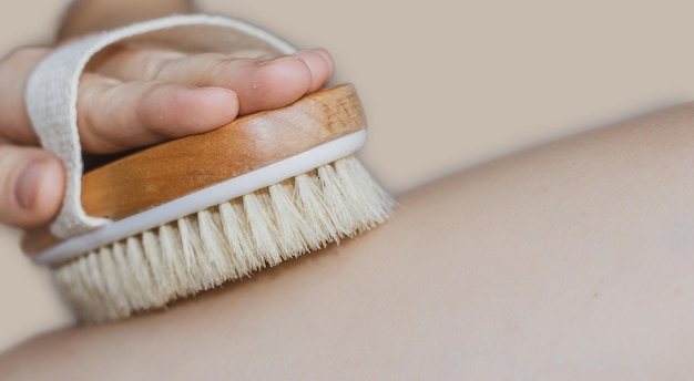 Frau verwendet Bürste für Trockenmassage warme Farbe beige Hintergrund Bürste für trockenen Körper gut zum Reduzieren